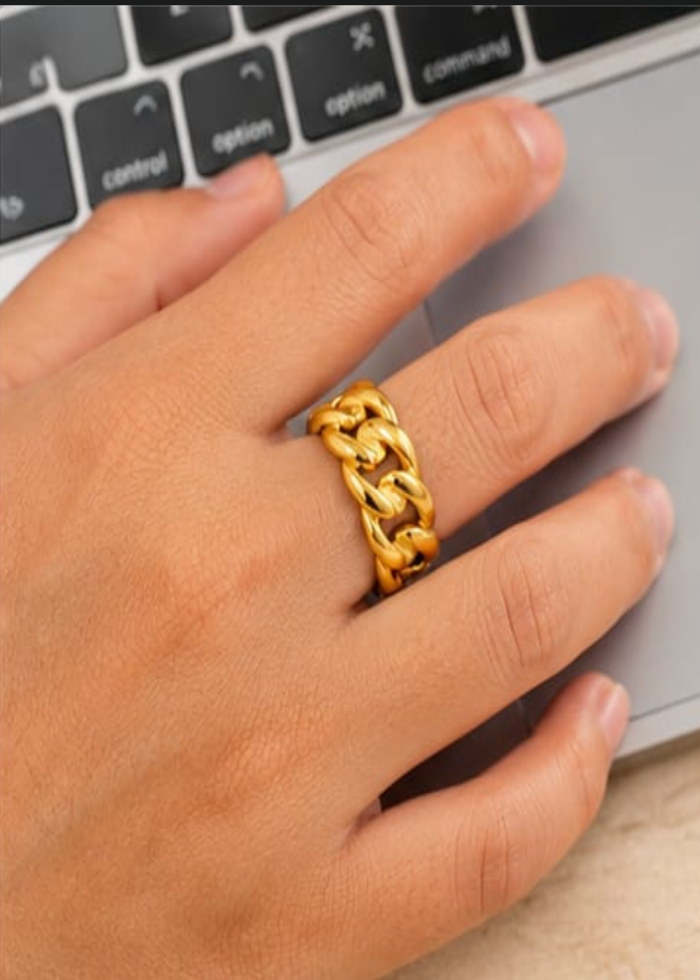 Hand wearing a gold chain ring on a laptop keyboard