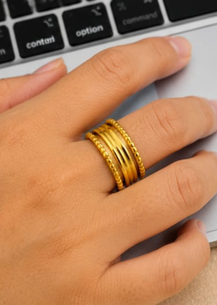 Hand wearing a gold ring with a laptop in the background